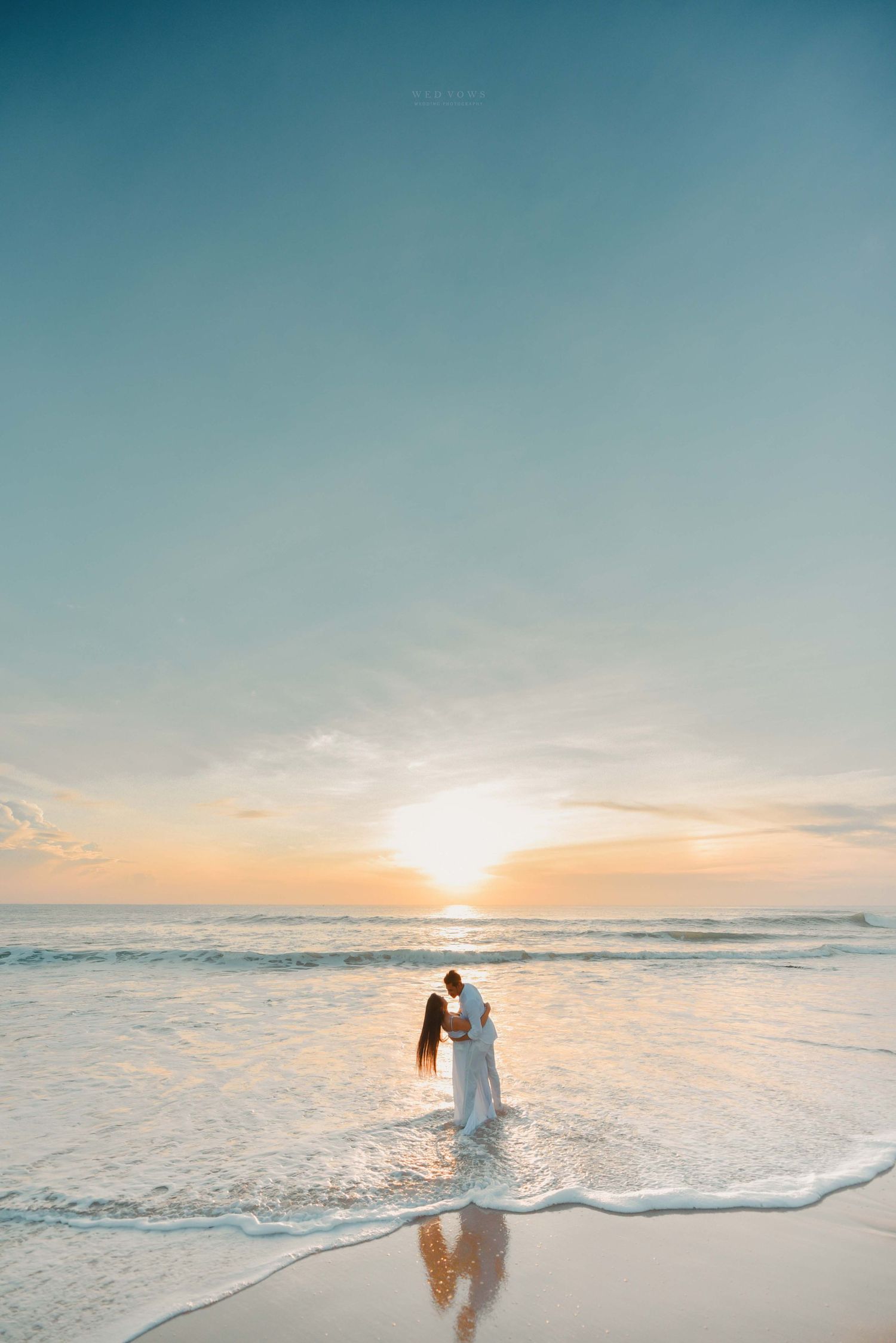 Bride and groom standing in ocean waves at sunset during beach wedding ceremony.