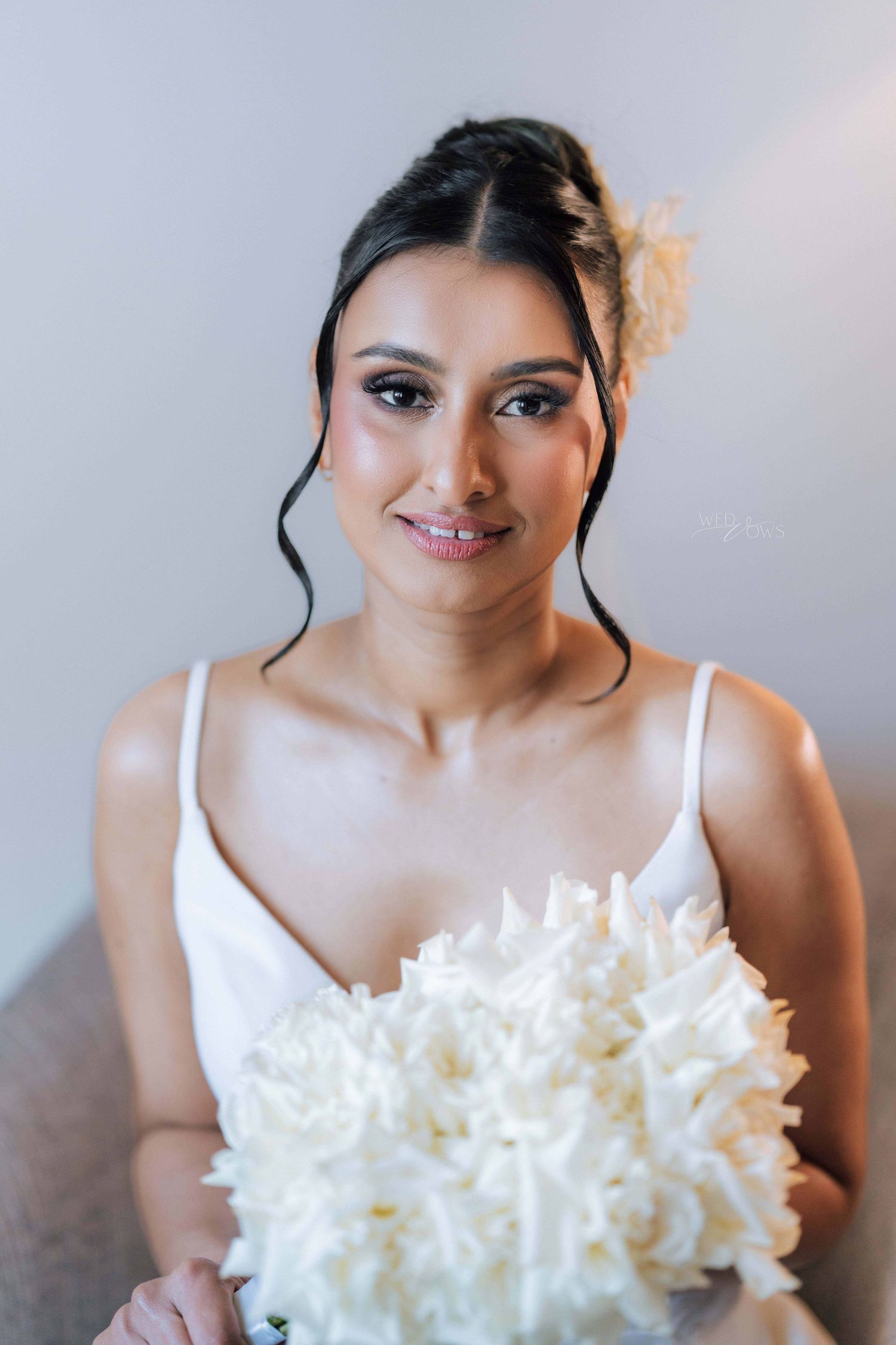Beautiful bride in white gown holding white floral bouquet with elegant updo hairstyle.
