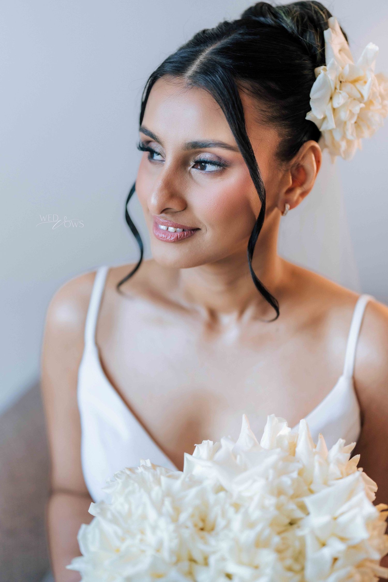 Beautiful bride with updo hairstyle holding large white peony bouquet in soft natural light.
