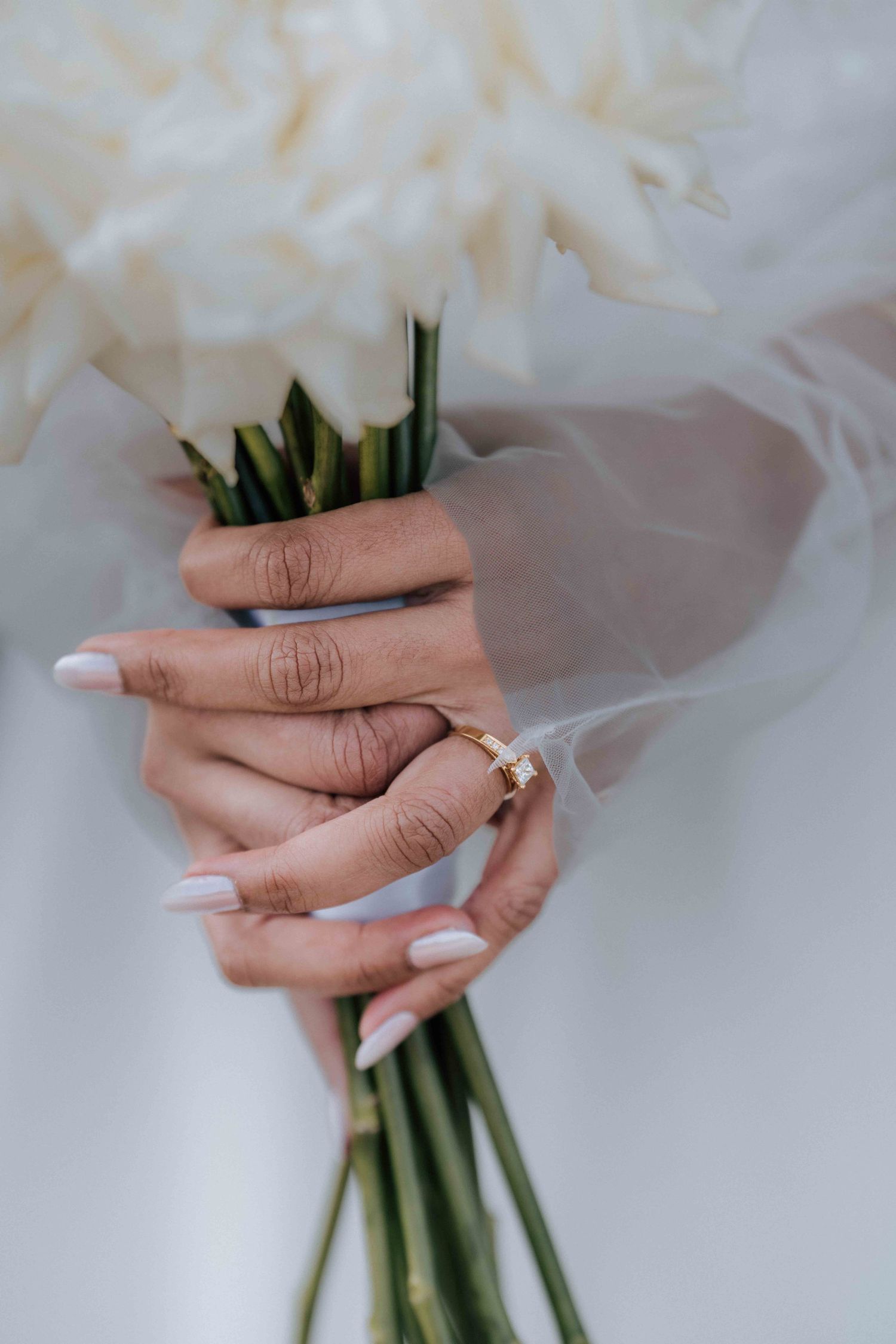 Close-up of bride holding white rose bouquet with gold diamond engagement ring and white manicured nails.
