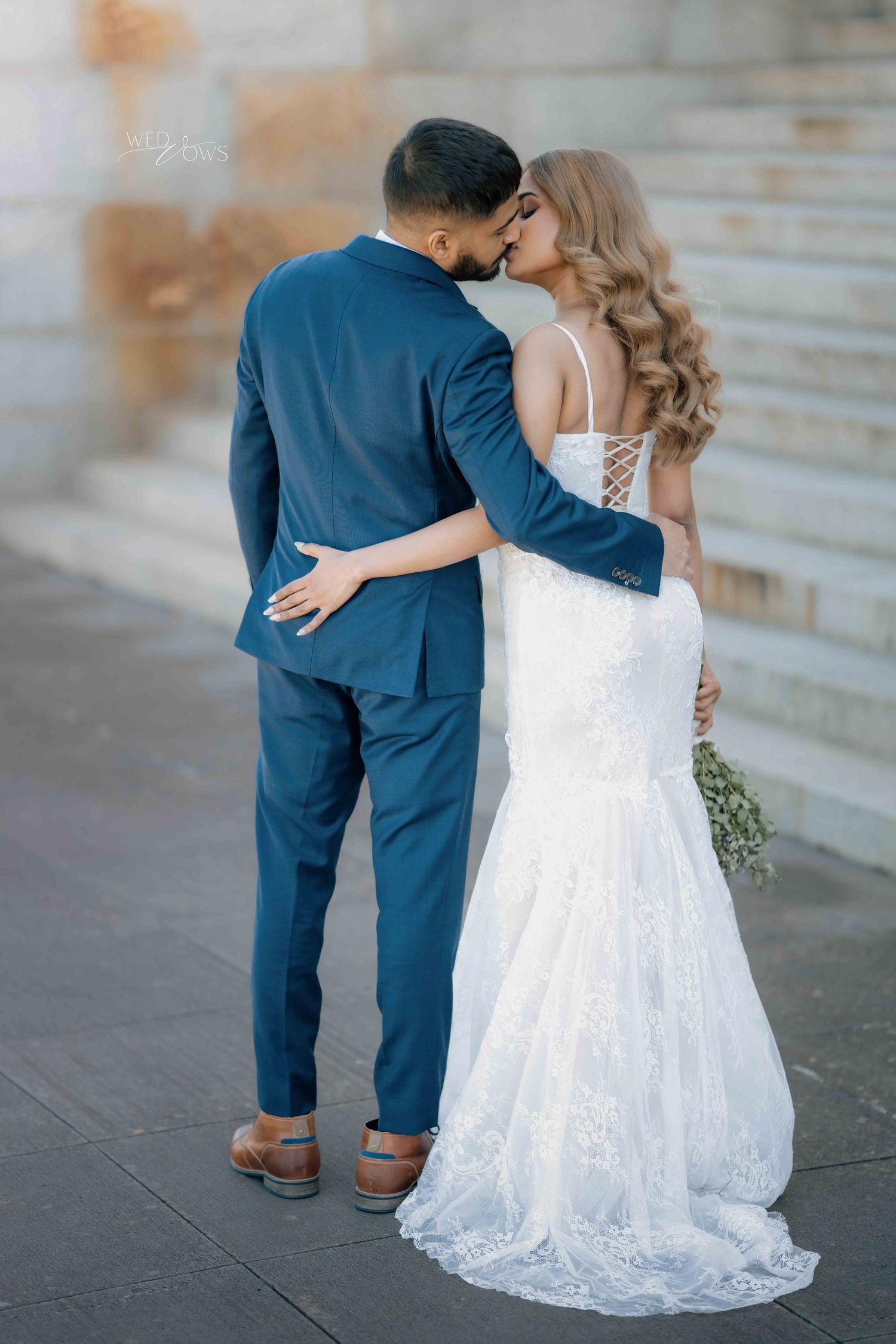 Bride and groom share a romantic kiss outdoors in elegant wedding attire.