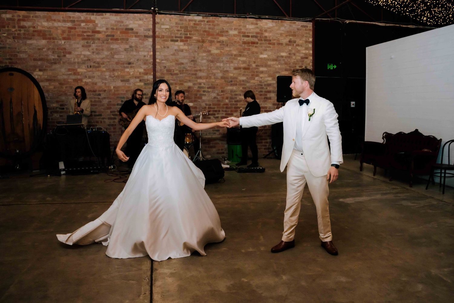 Bride and groom share first dance in rustic venue with exposed brick walls and wood floors.