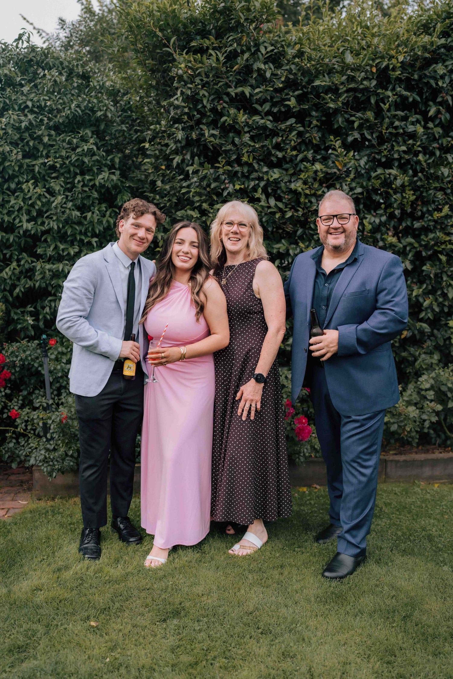 Family of four in formal attire pose together on a lawn at a wedding reception.