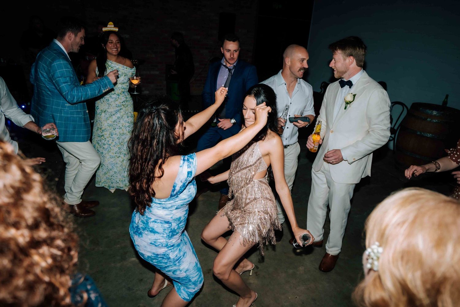 Guests dancing energetically at a lively wedding reception party in a dimly lit venue.