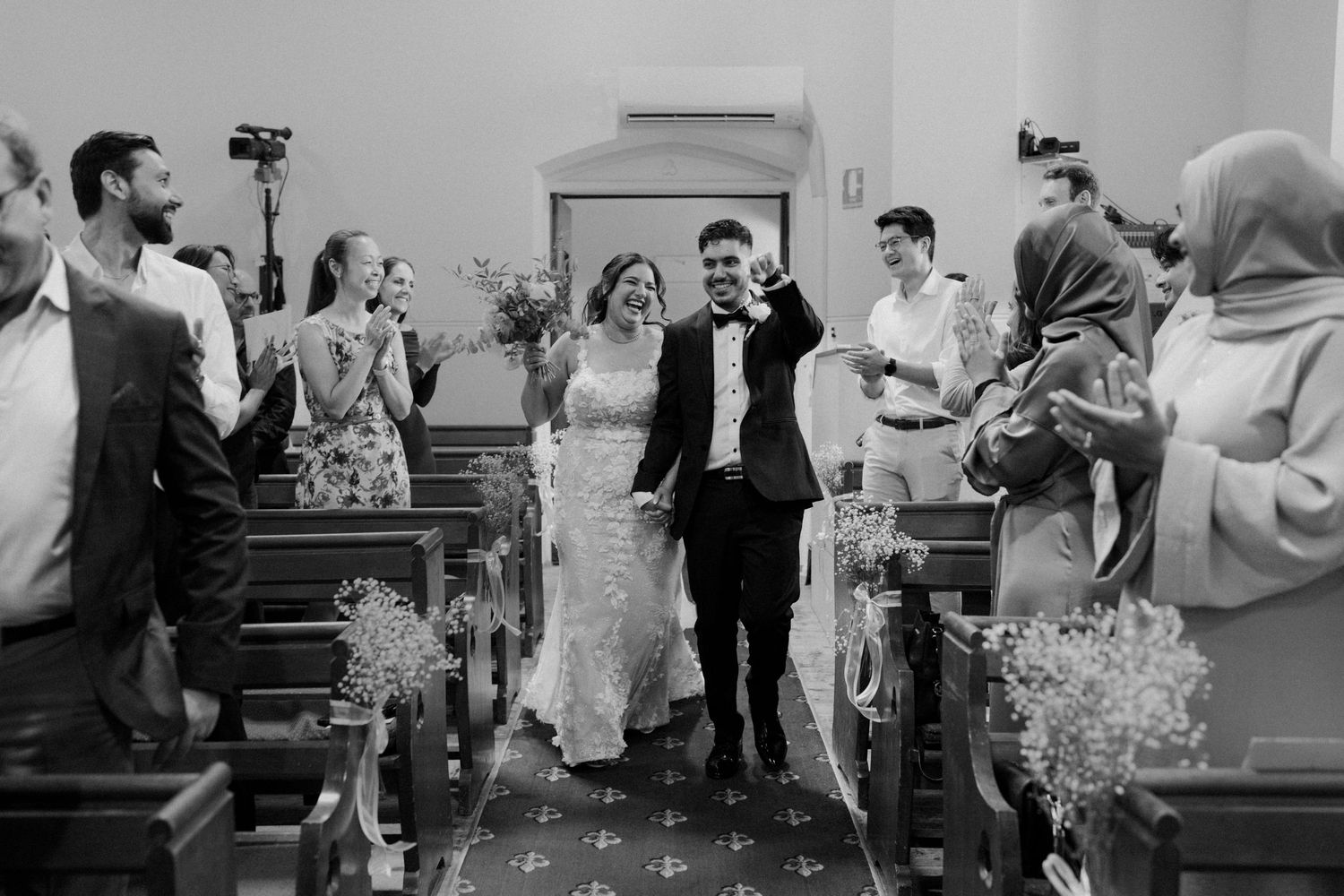 Black and white photo of joyful bride and groom walking down church aisle after ceremony.