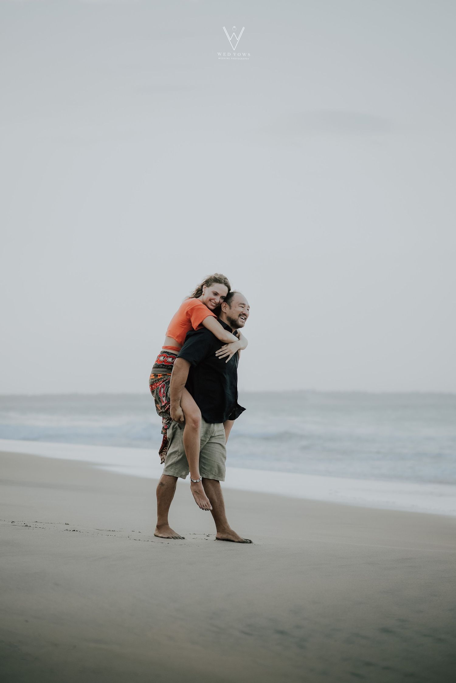 Playful couple on beach, man giving woman a piggyback ride along the shoreline.