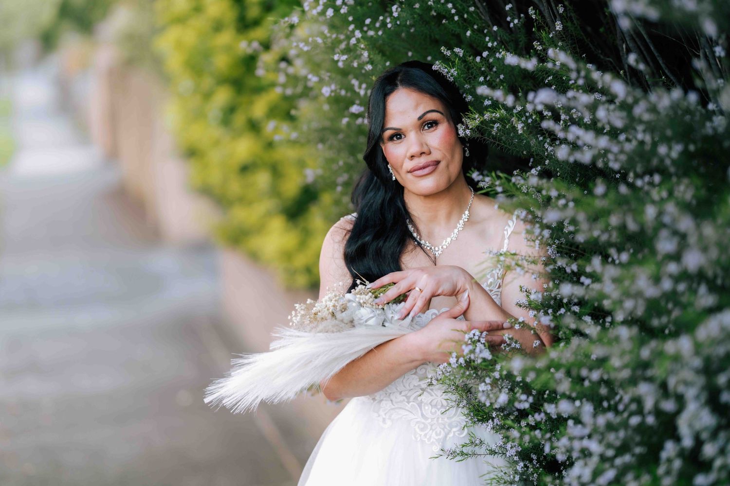 Bride in a white wedding gown holding a feather bouquet surrounded by blooming white flowers.