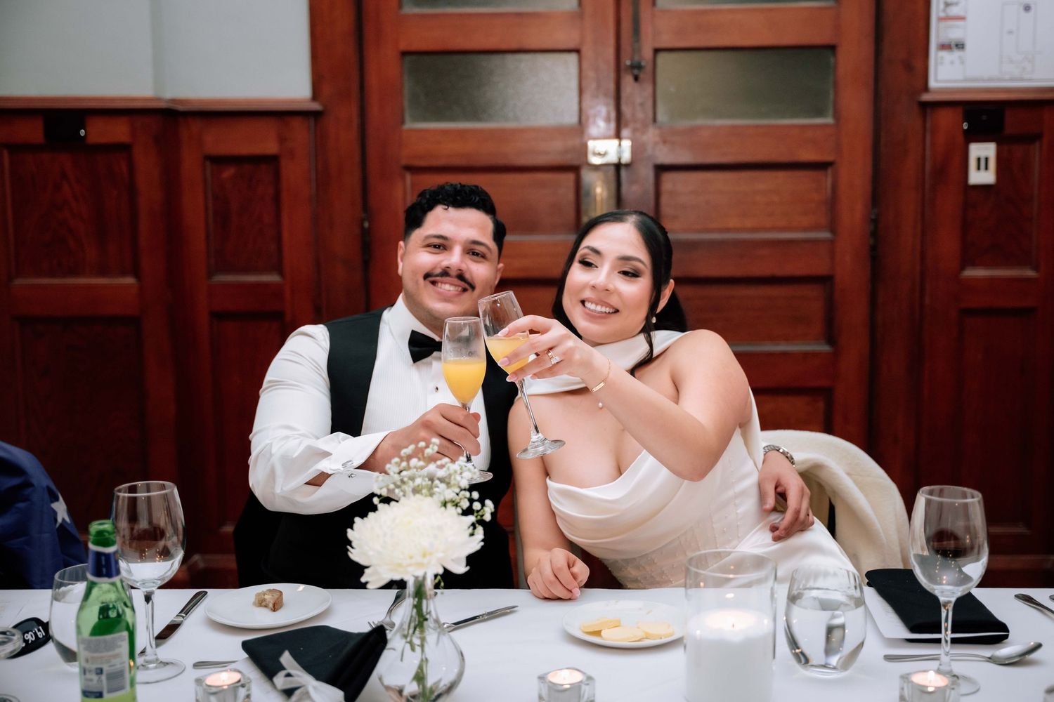 Bride and groom smiling and toasting with mimosas at their wedding reception dinner table.