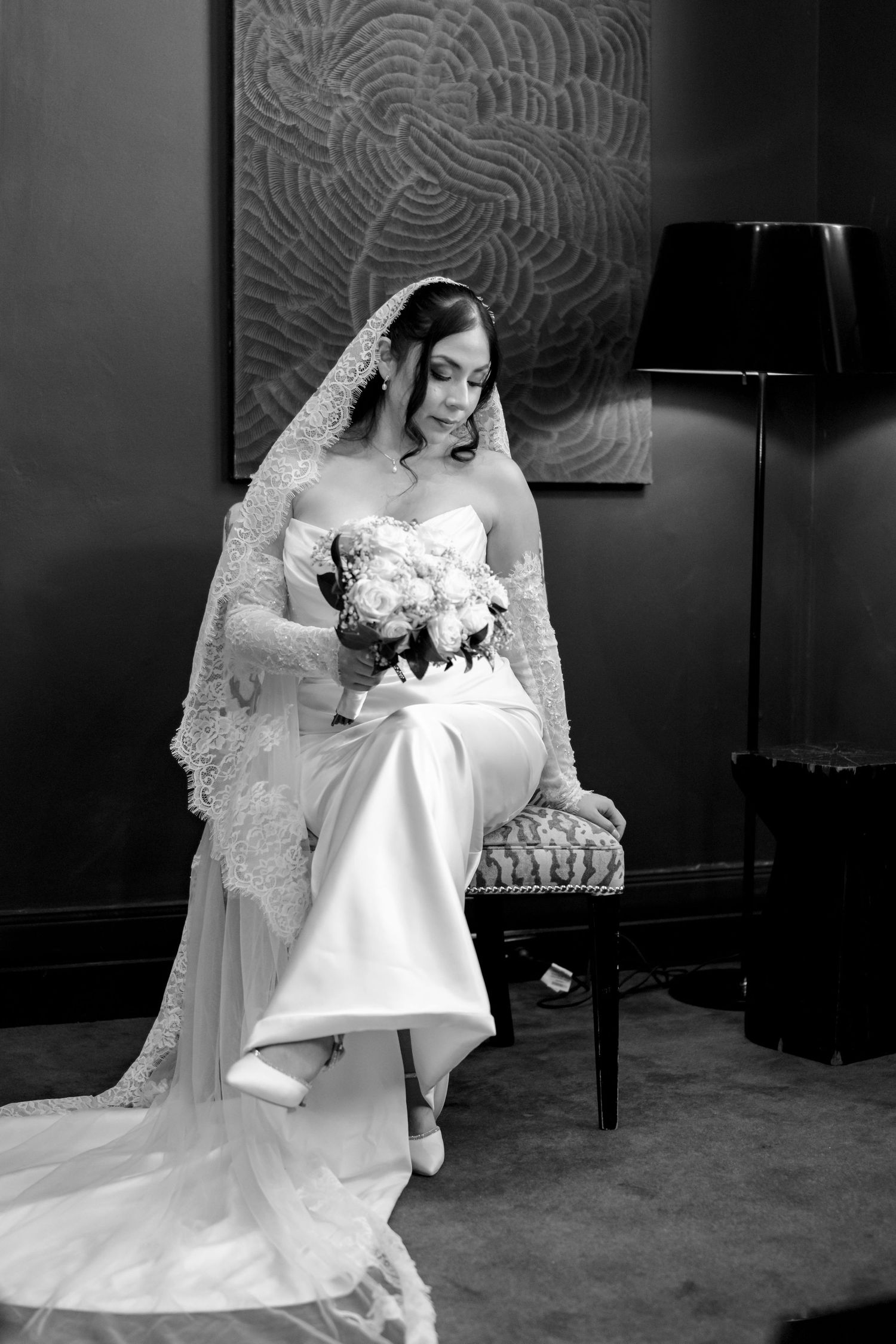 Black and white portrait of an elegant bride in a lace veil holding a bouquet while seated.