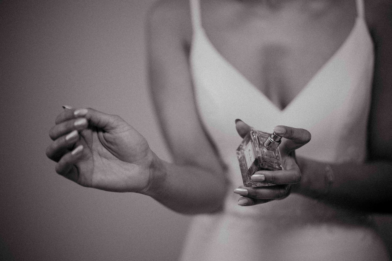 Black and white photo of a bride in white lingerie holding a perfume bottle elegantly.