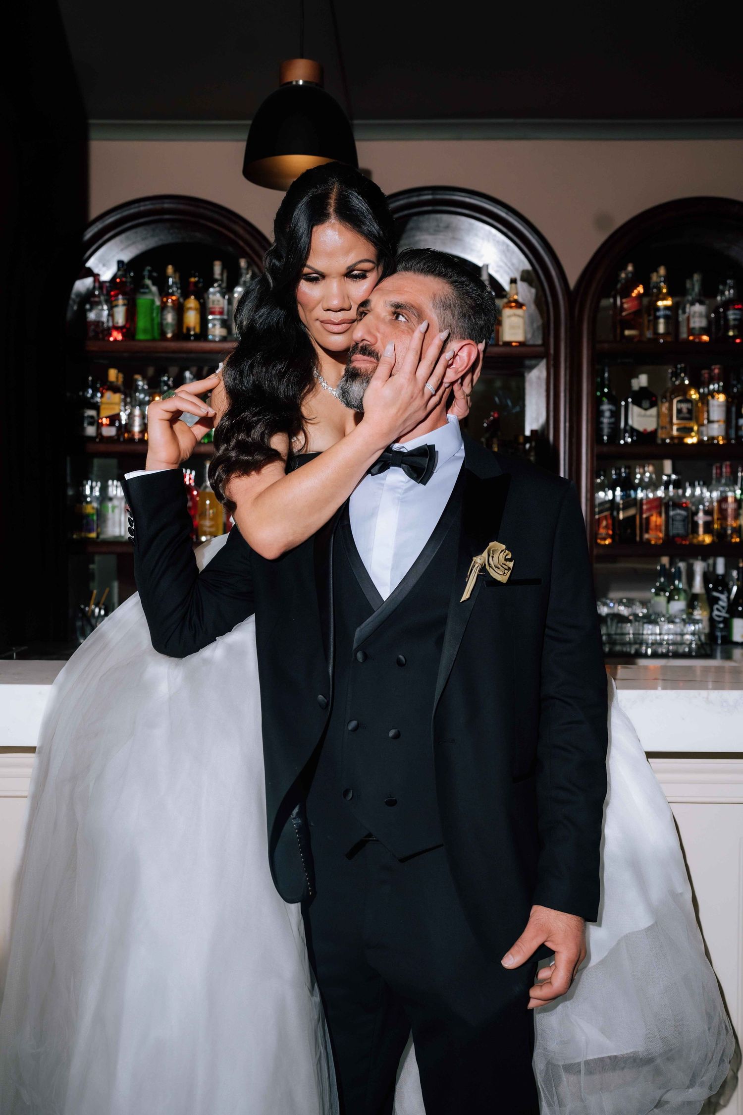 Bride and groom sharing a romantic moment at a bar, bride tenderly holding grooms face in her hands.