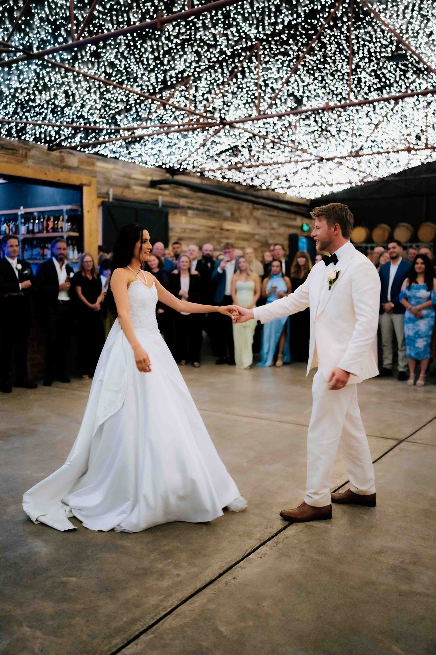 Bride and groom share first dance under twinkling fairy lights in a rustic winery venue.