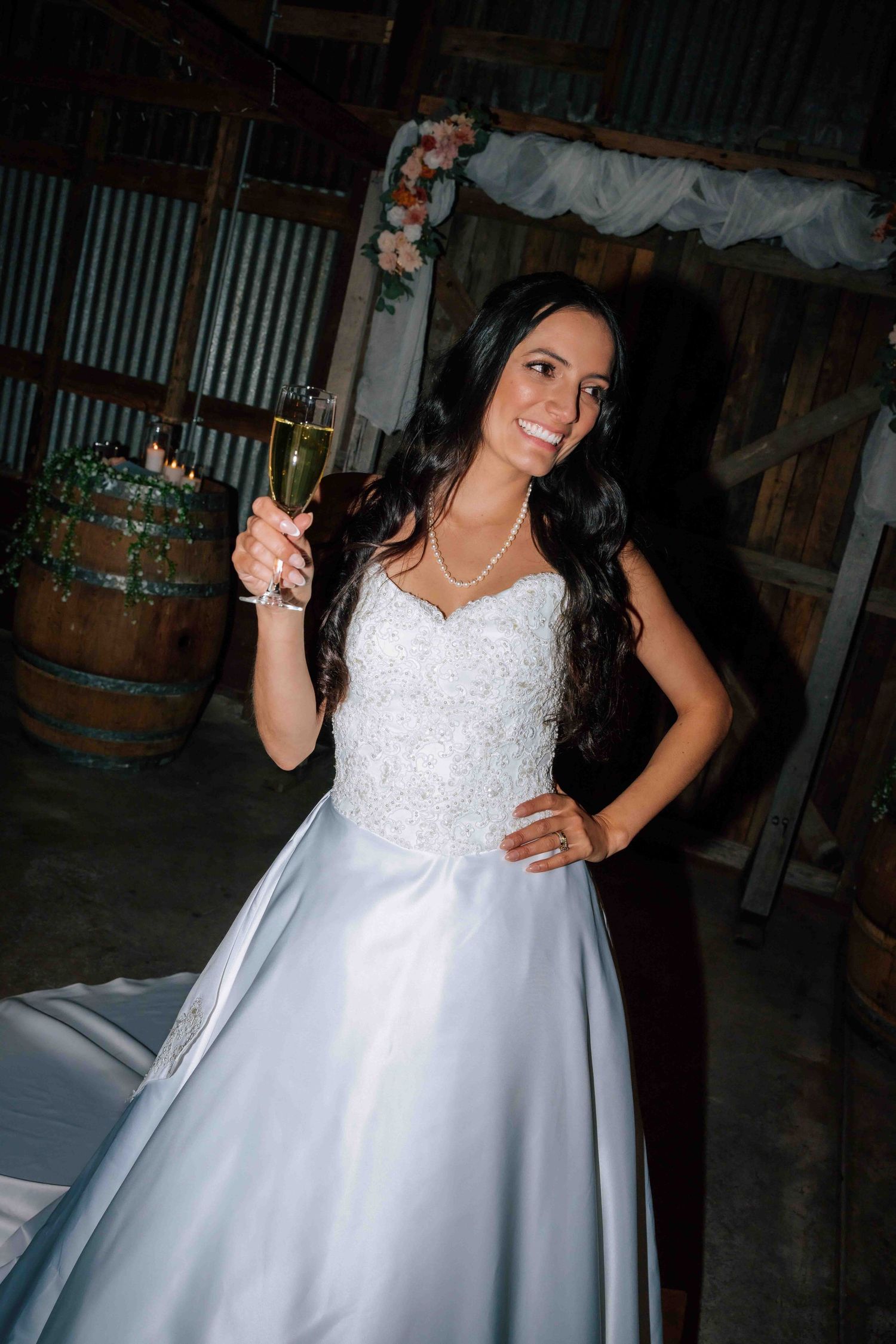 Radiant bride in white ball gown toasting with champagne glass at rustic barn wedding reception.