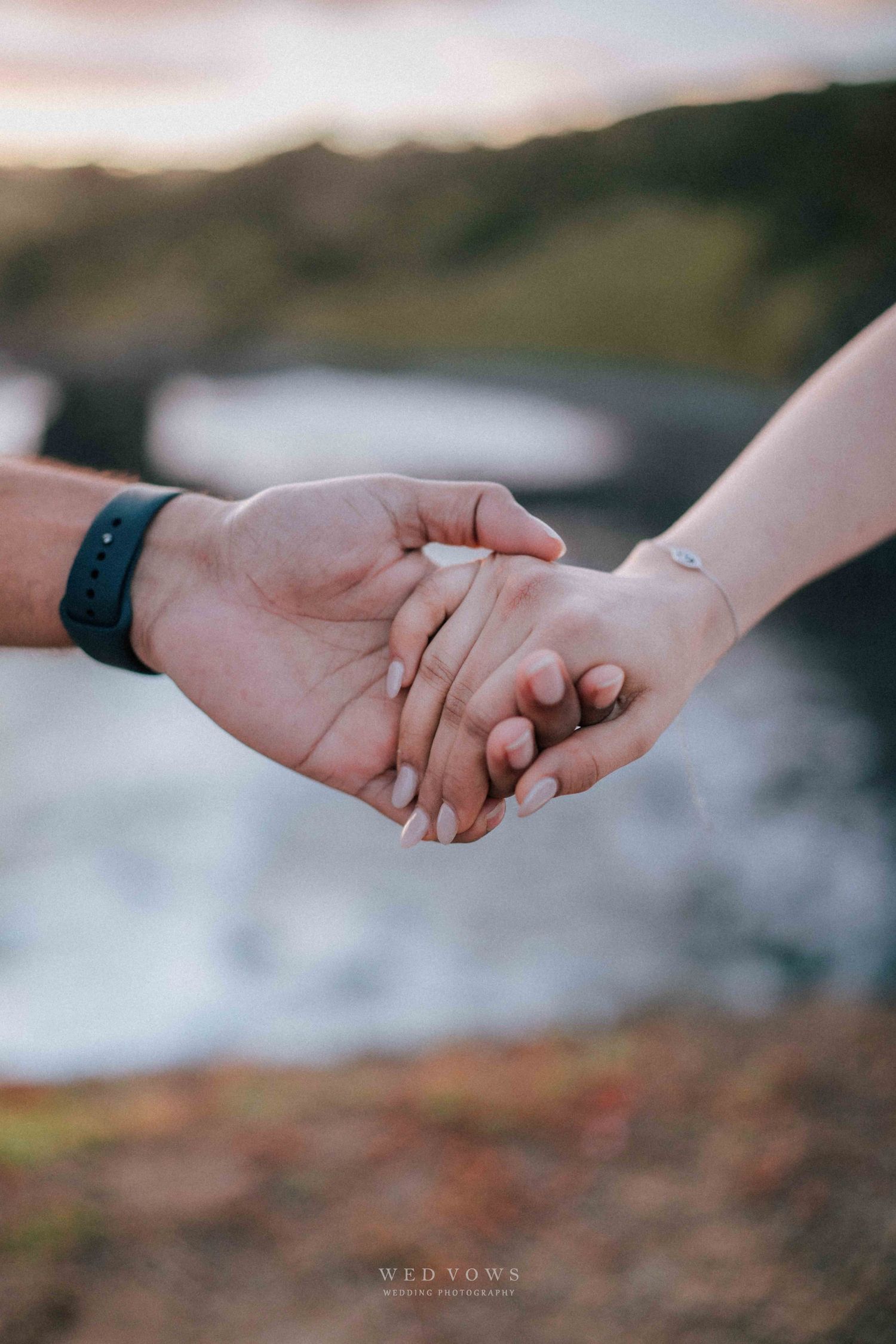 Close-up of a couple holding hands tenderly near the ocean at sunset.