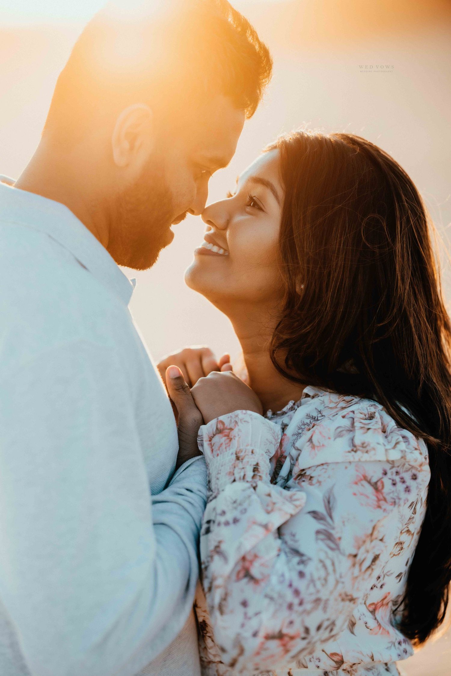Smiling couple gazing at each other tenderly in warm golden sunset light on the beach.