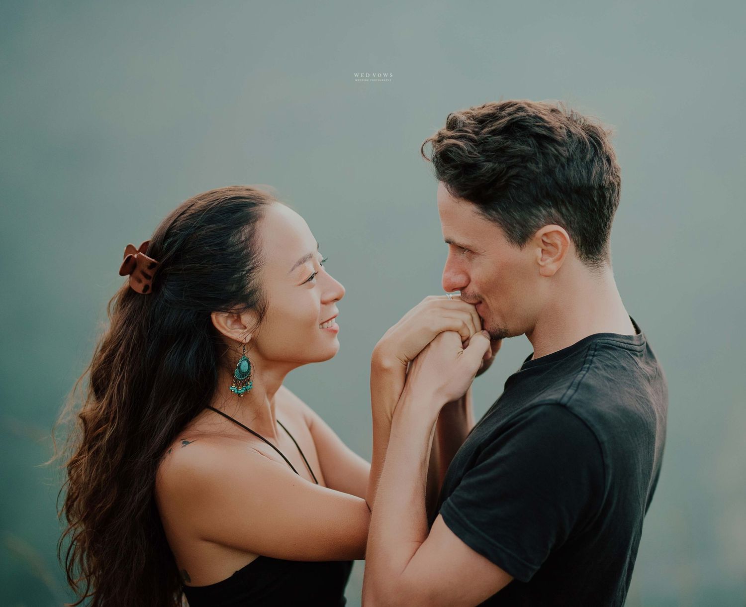 A romantic couple sharing a tender moment as the man gently kisses the womans hand while she smiles.