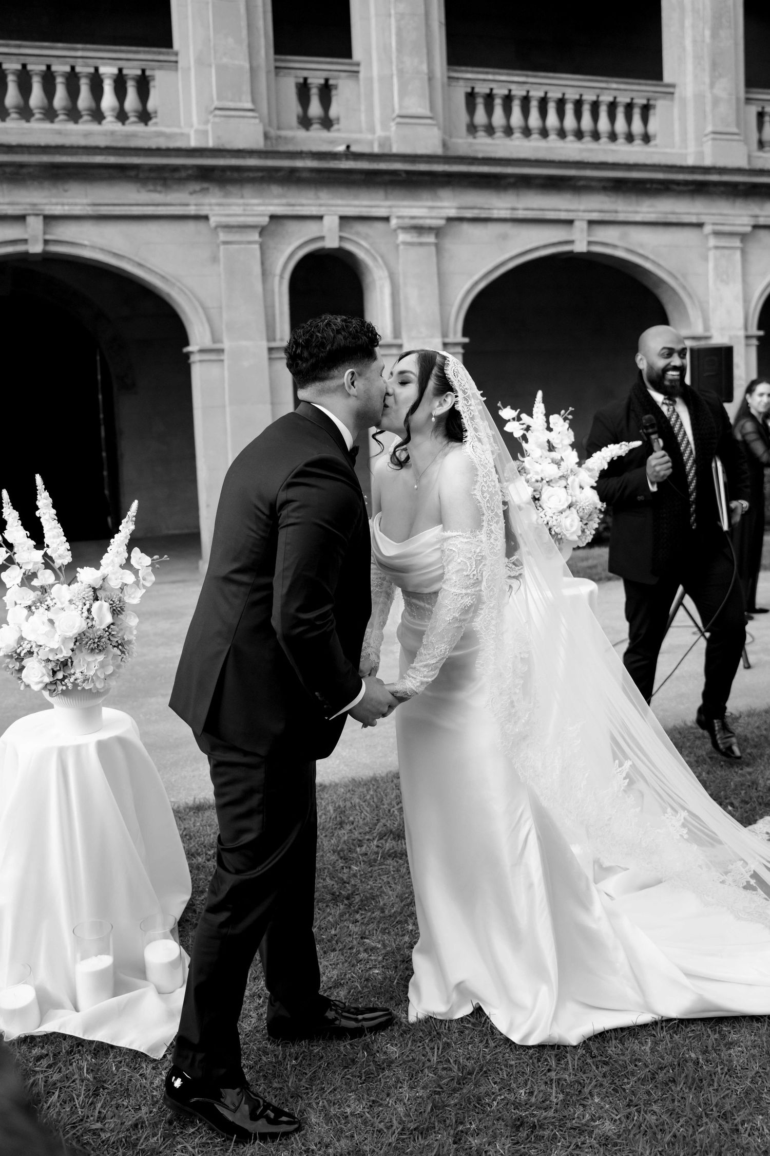 Bride and groom share first kiss at outdoor wedding ceremony in black and white photo.