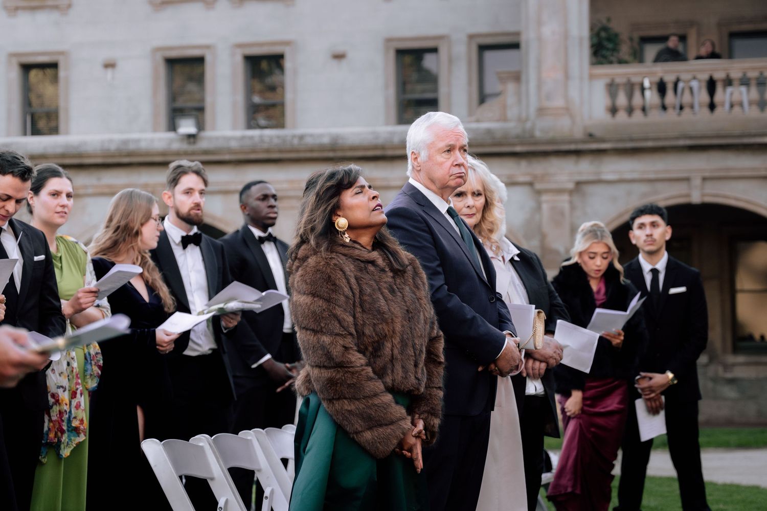 Wedding guests standing and reading during an outdoor ceremony at a historic estate venue.