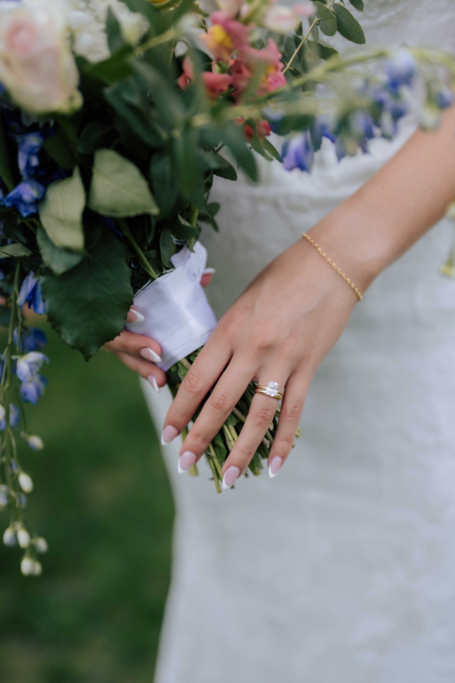 Close-up of brides hand holding bouquet showing gold diamond engagement ring and bracelet.