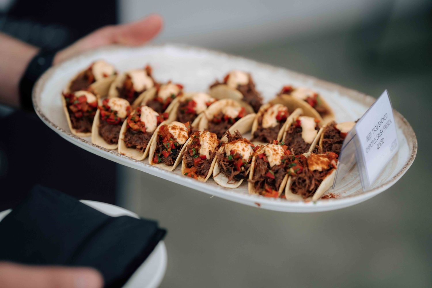 A server presenting a platter of elegant mini tacos as wedding reception appetizers at an event.