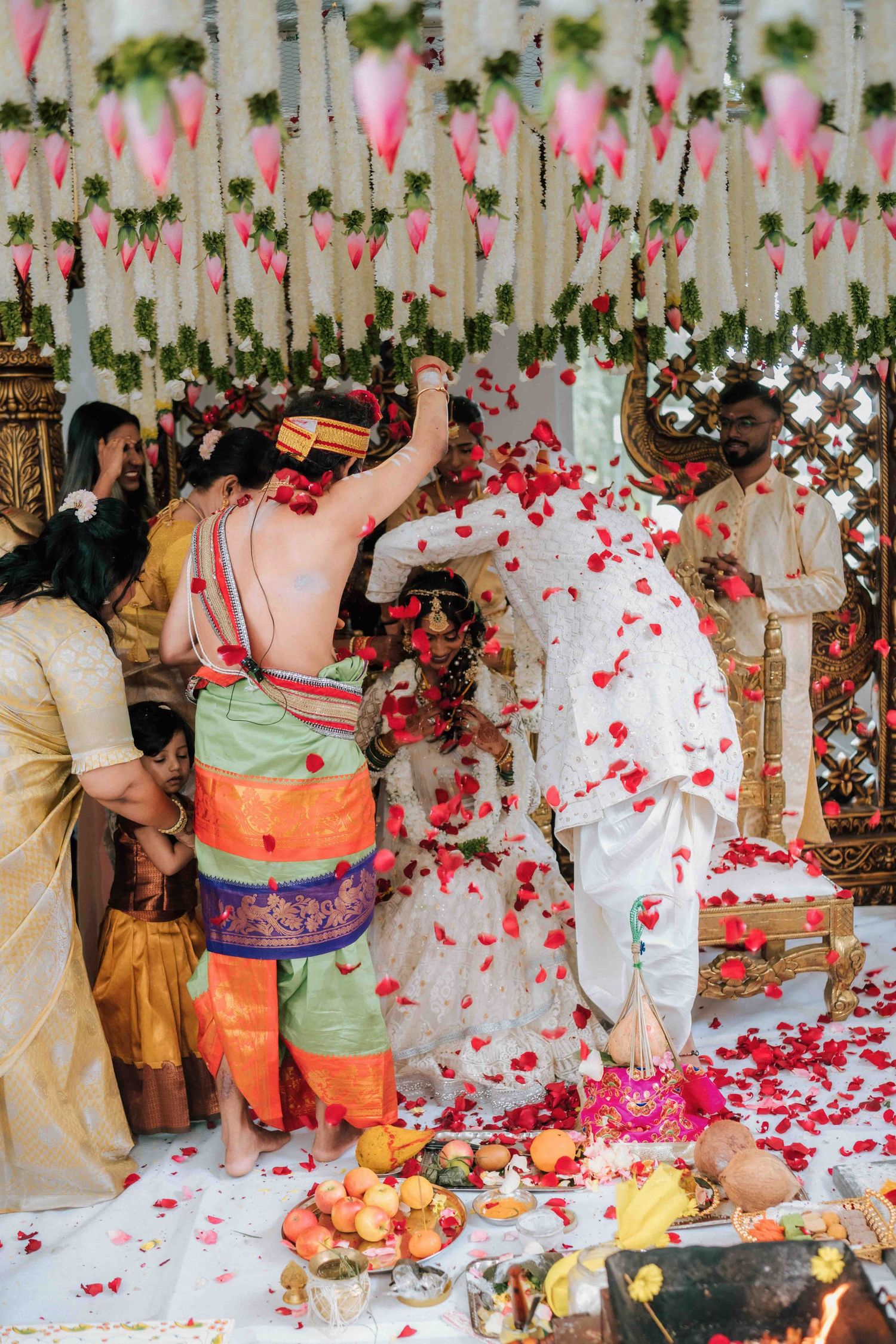 Rose petals shower over a couple during a vibrant Hindu wedding ceremony with floral decorations.
