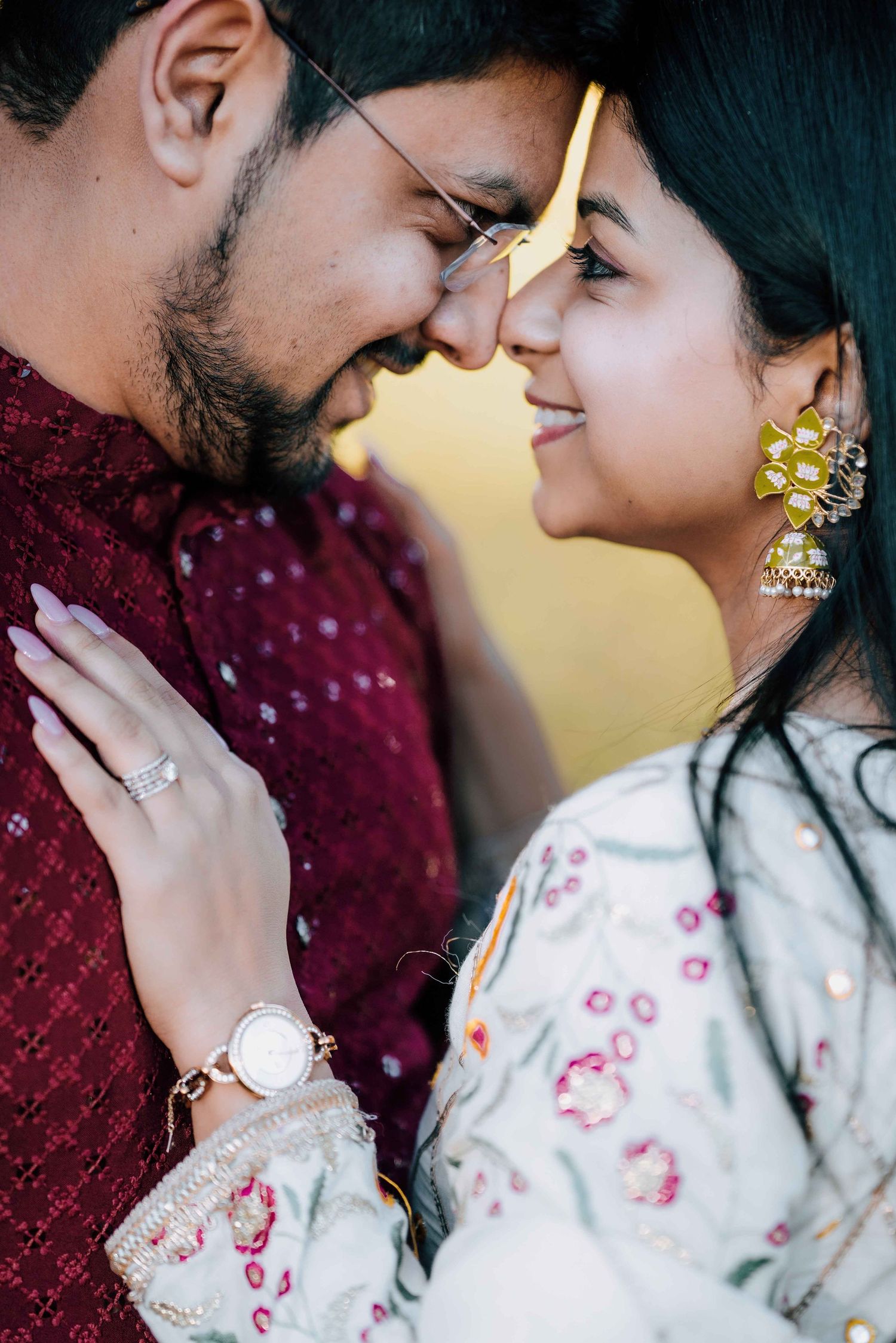 Close-up of South Asian couple touching foreheads, woman wearing gold jhumka earrings.