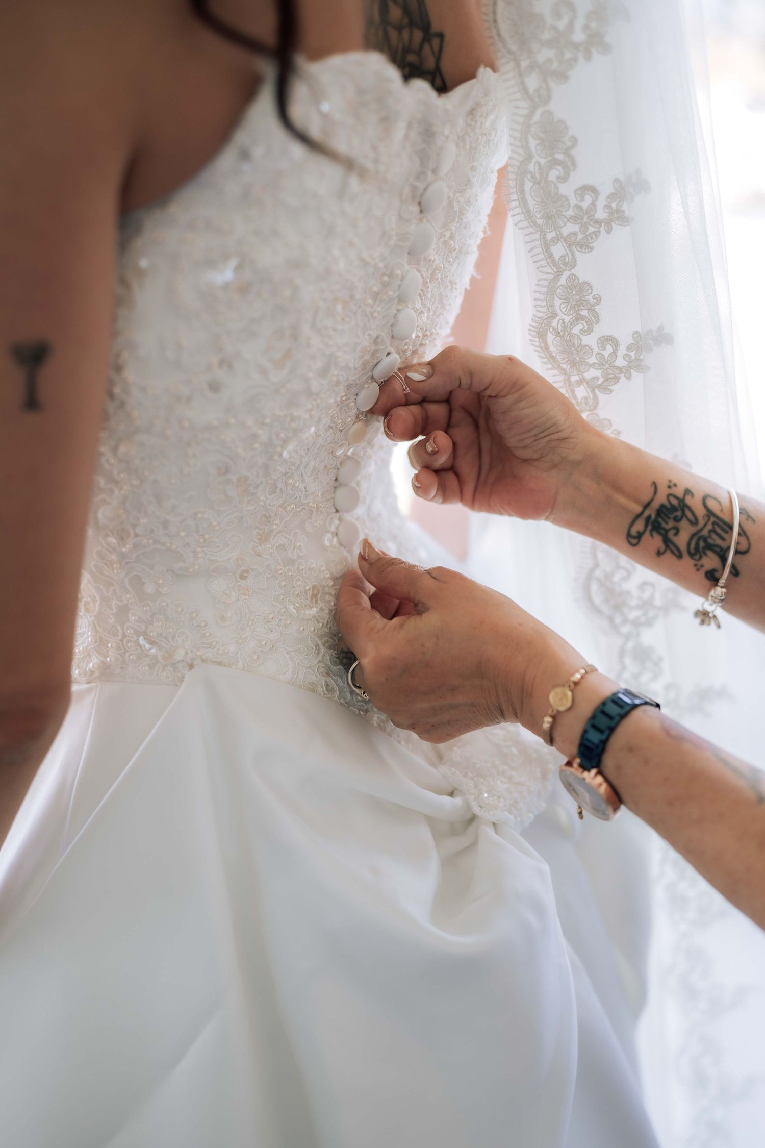 Hands with tattoos fastening buttons on back of white lace wedding dress.