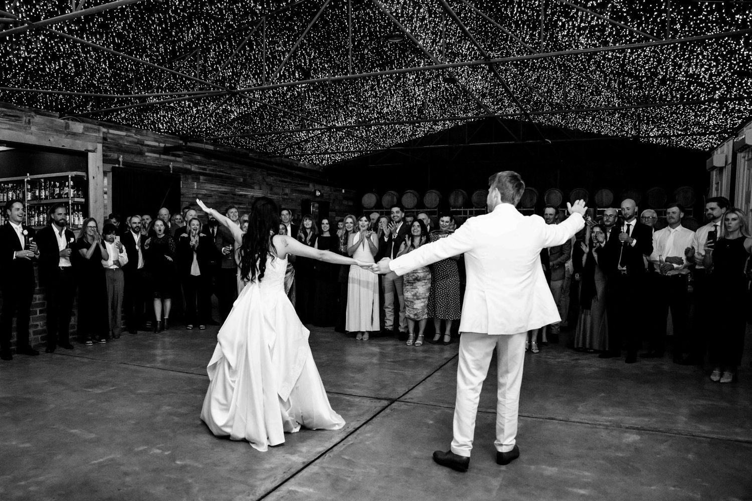 Black and white photo of bride and groom sharing first dance under twinkling lights at reception.