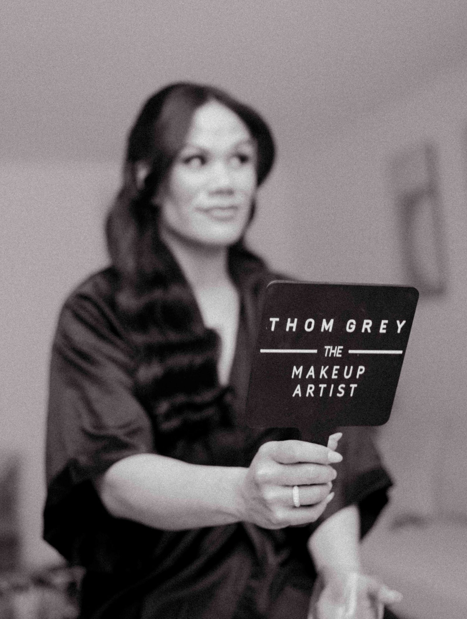 Black and white photo of a bride holding a Thom Grey makeup artist sign during bridal prep.