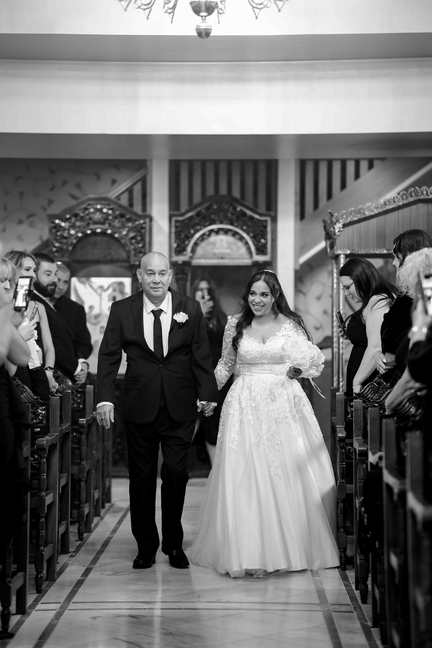 Bride in lace gown walks down church aisle with father during wedding ceremony.
