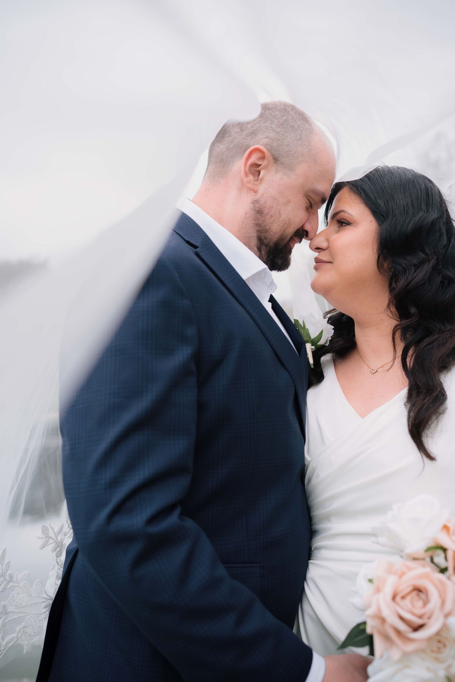 Bride and groom share an intimate forehead touch framed by a flowing white wedding veil.