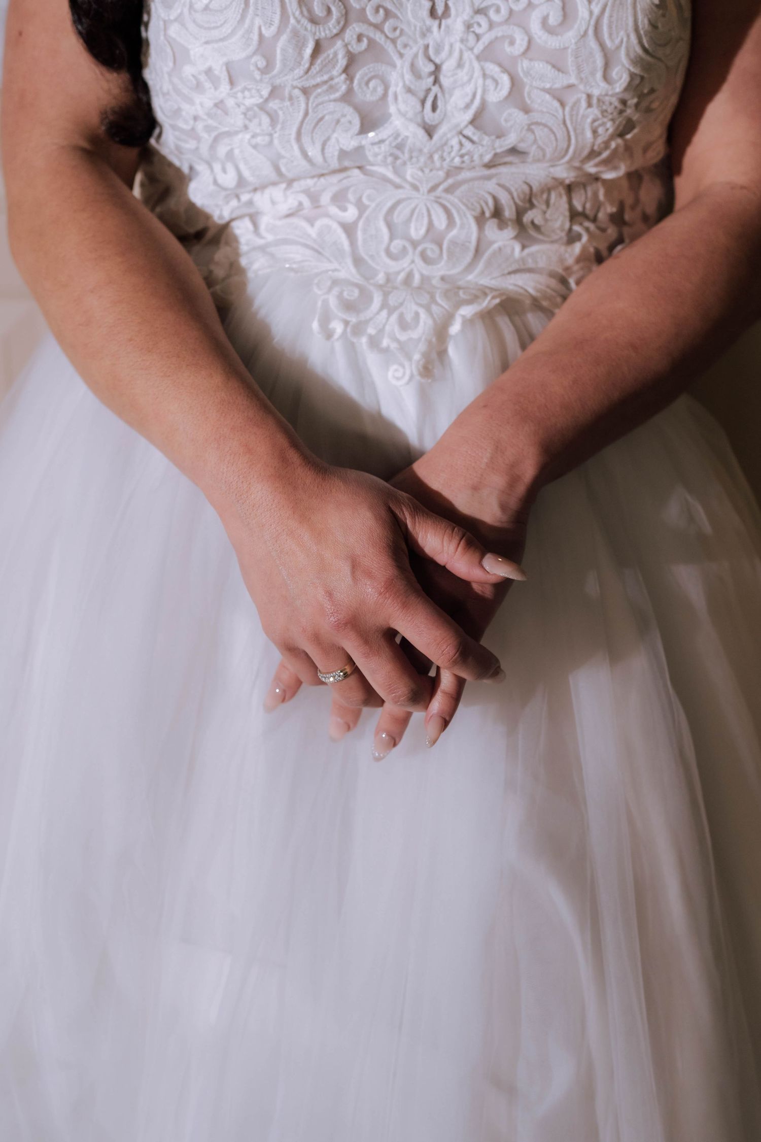 A close-up of a bride's hands clasped together showing a diamond engagement ring on her wedding day.
