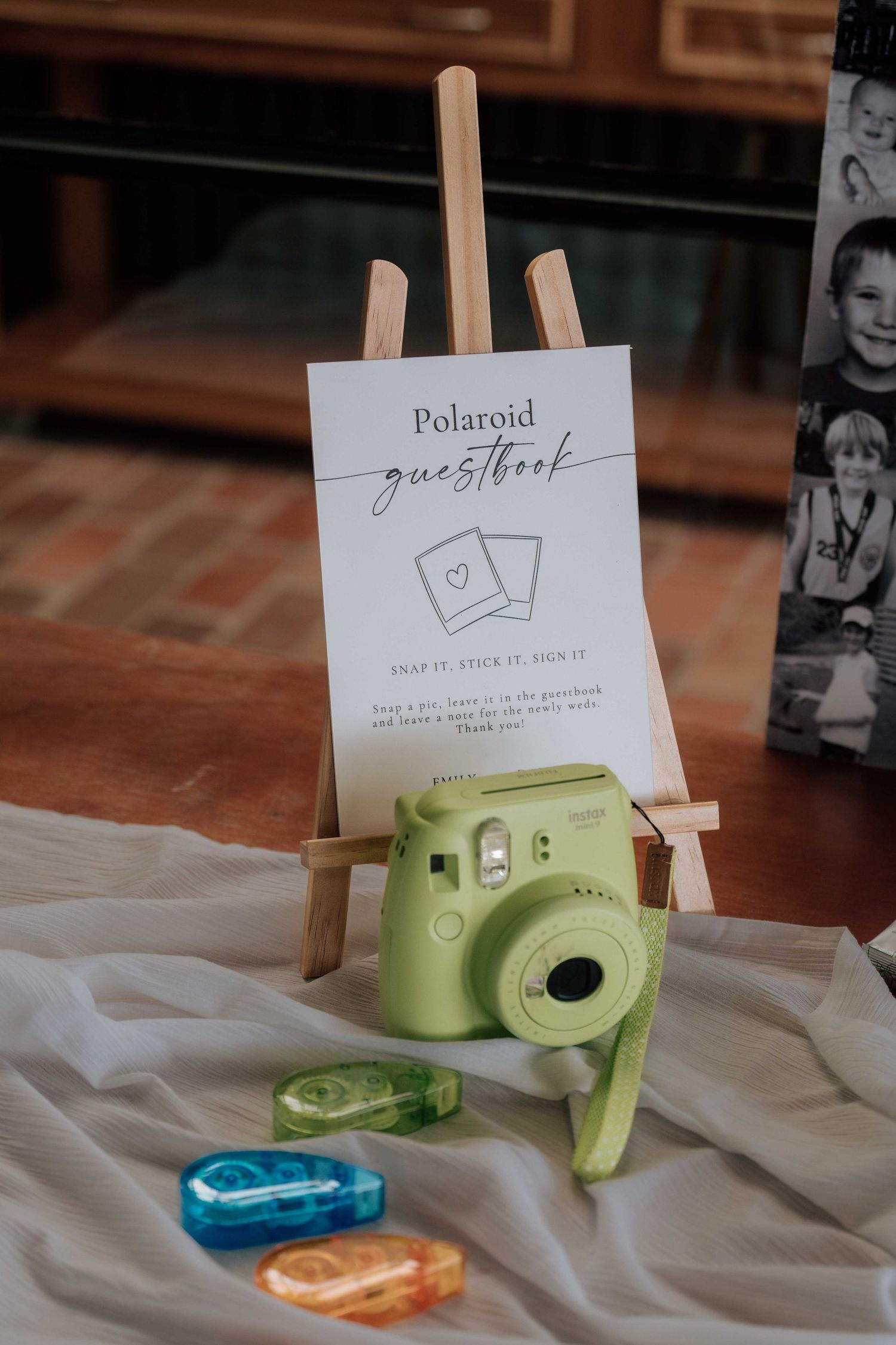 Green Polaroid camera beside a guestbook sign on an easel with colorful tape dispensers at a wedding.