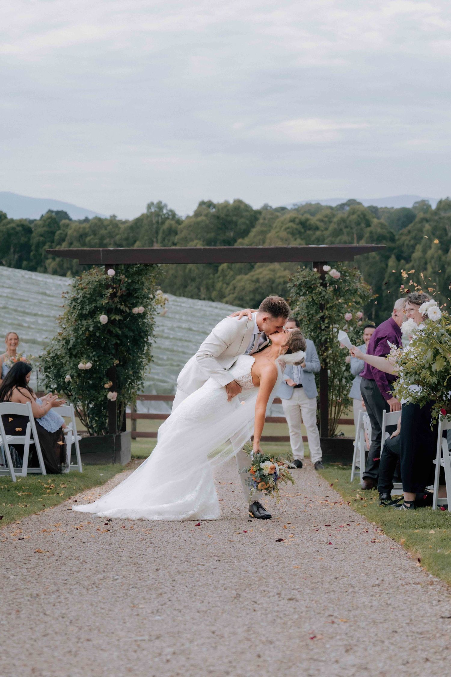Groom dips bride for a dramatic kiss at the end of the aisle during an outdoor vineyard wedding ceremony.