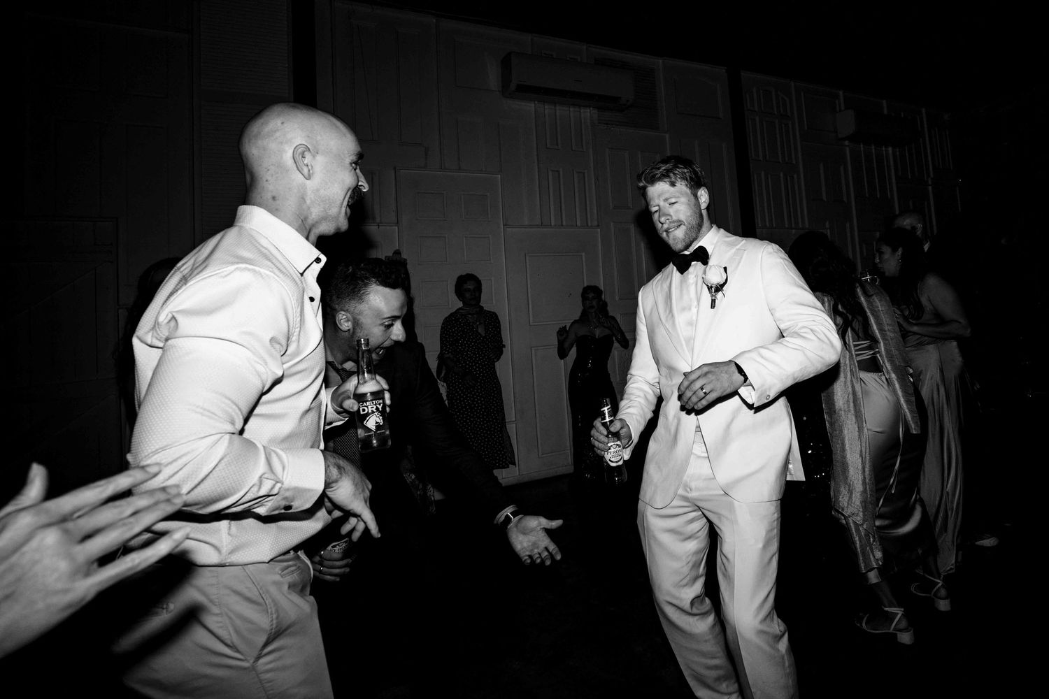 Black and white photo of groomsmen dancing and celebrating together on the wedding reception dance floor.