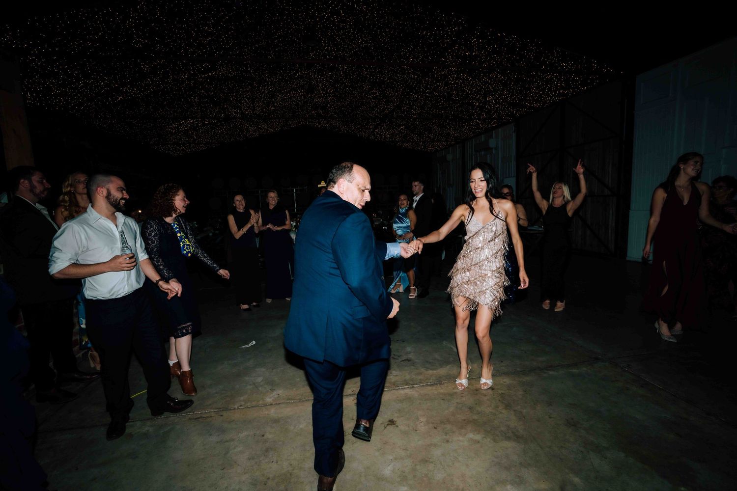 Wedding guests dancing energetically on a dark dance floor during a lively wedding reception celebration.