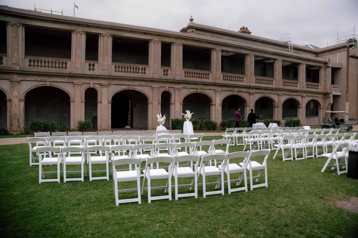 White chairs arranged on lawn for outdoor wedding ceremony at historic stone building.