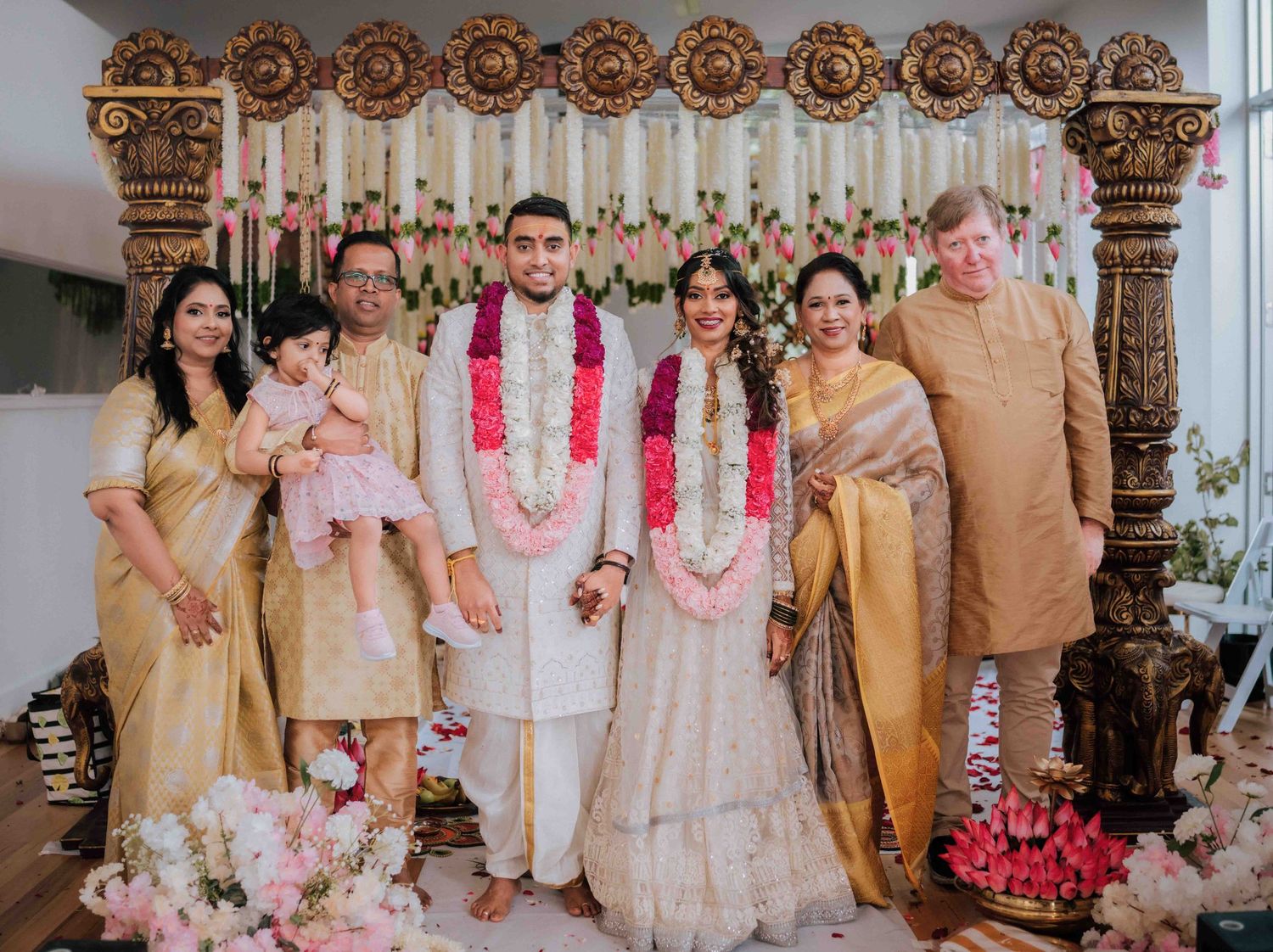 Indian wedding family portrait with bride, groom, and extended family standing before a grand decorated golden mandap.