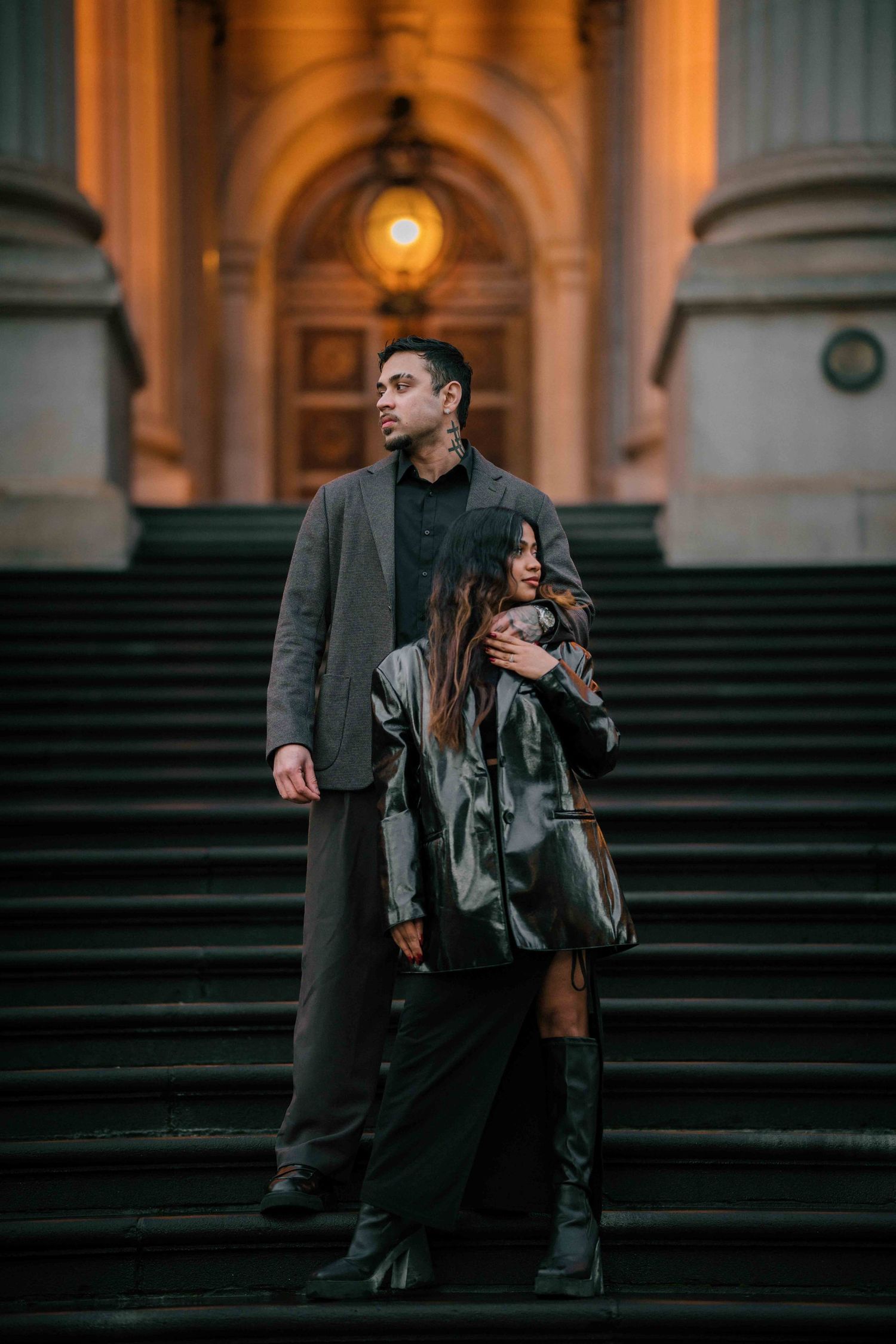 Couple standing together on steps of a grand illuminated historic building at night.