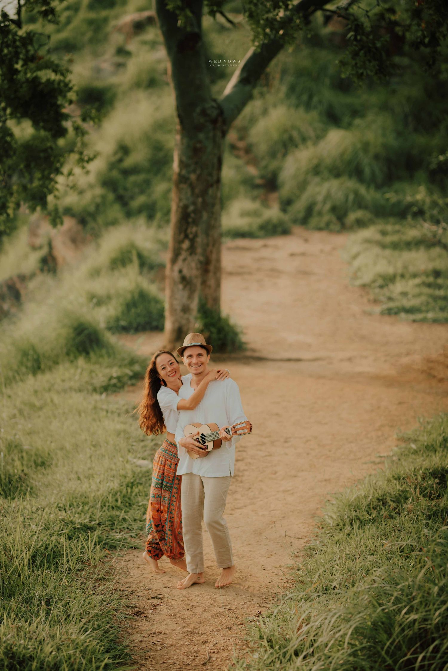 Couple embracing on a sunlit dirt path through lush green forest with ukulele.