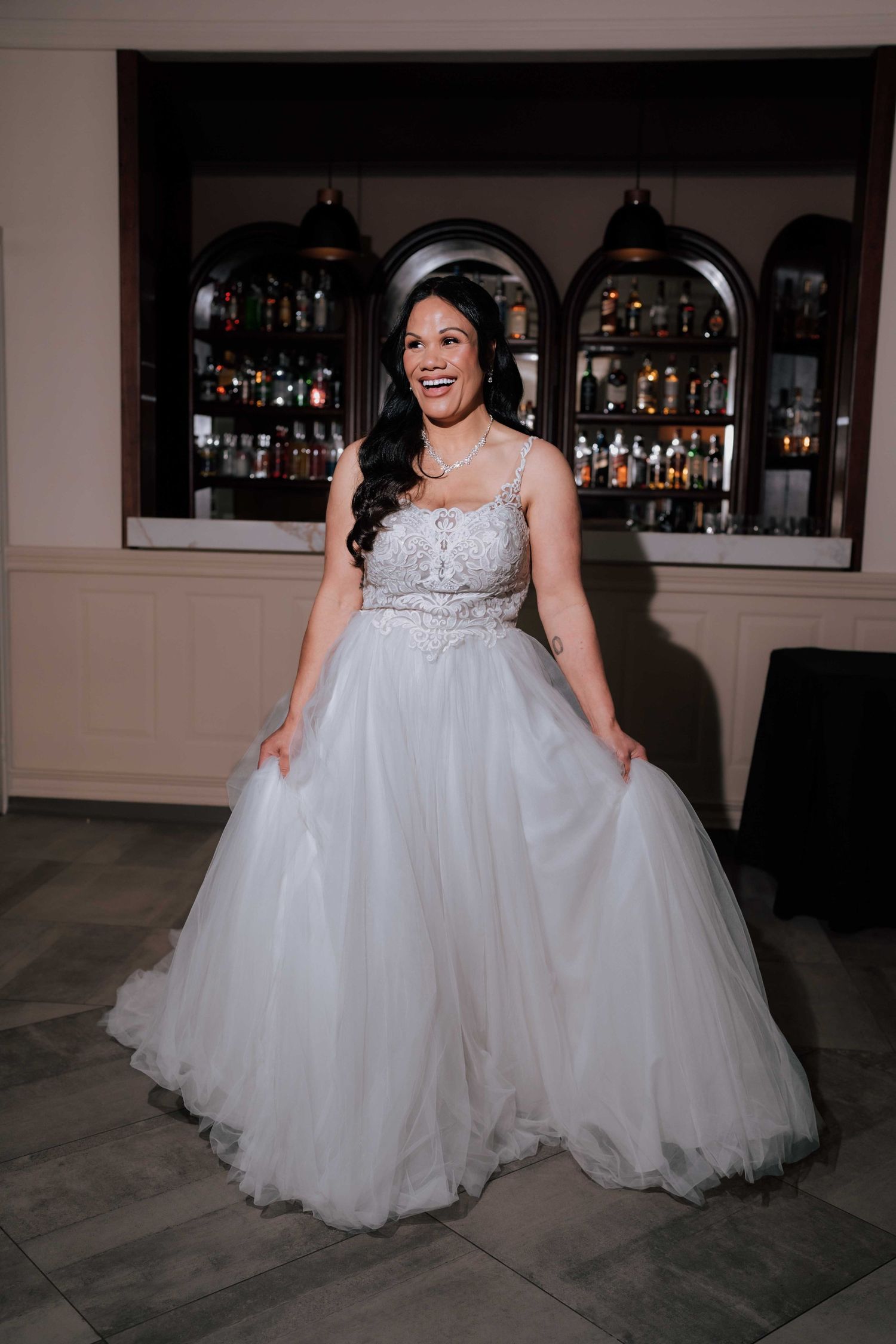 Smiling bride in beaded ballgown standing in front of bar at wedding reception.