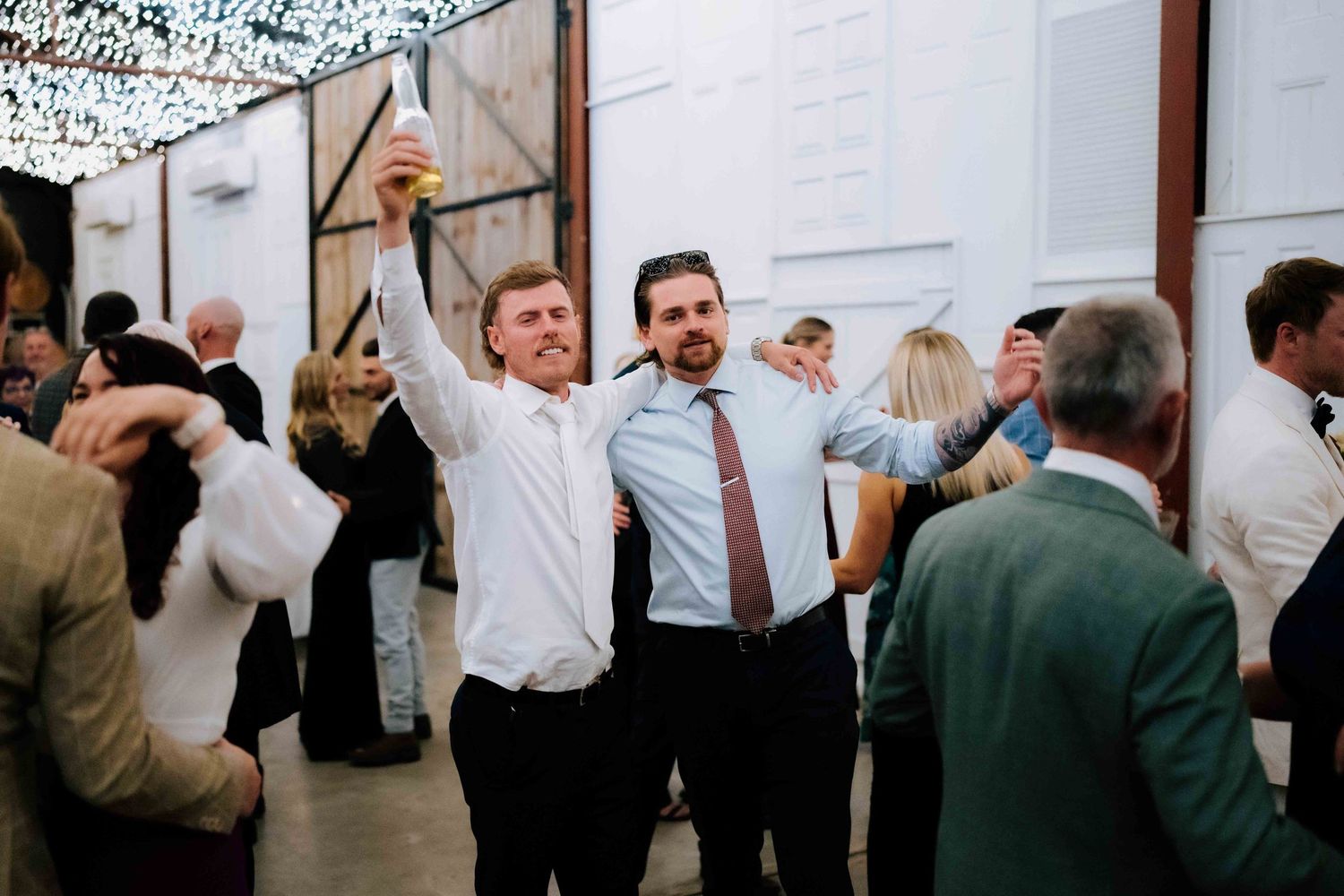 Wedding guests laugh and take selfies while dancing and celebrating at a lively indoor wedding reception.