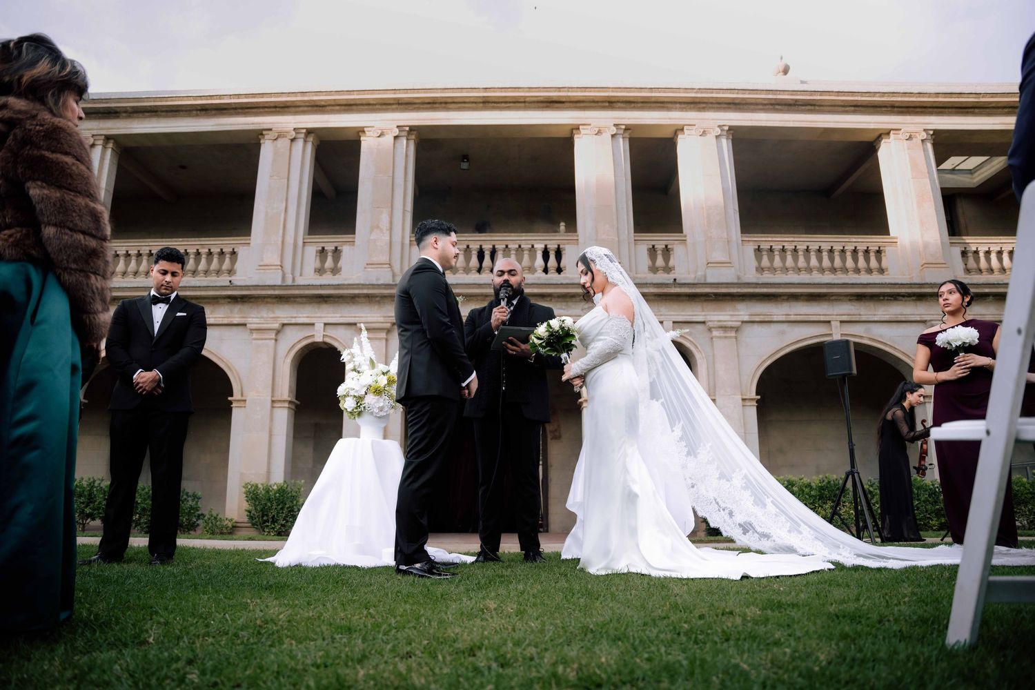 Outdoor wedding ceremony with bride and groom at altar before historic columned building.
