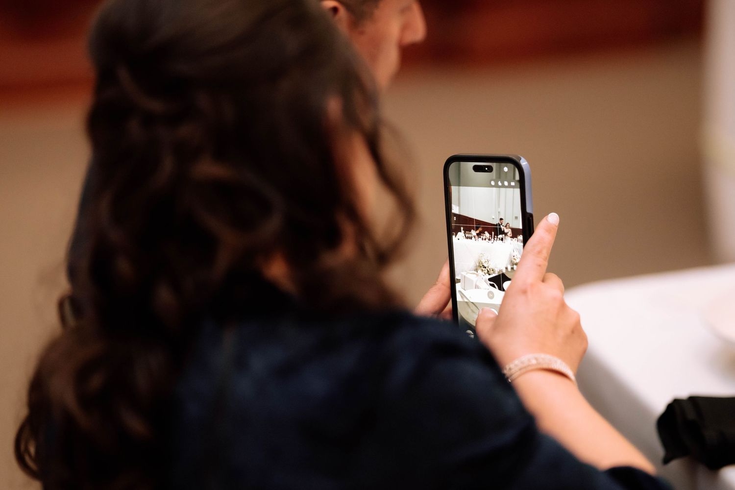 Wedding guest photographs reception moments on smartphone at elegantly decorated indoor wedding venue.