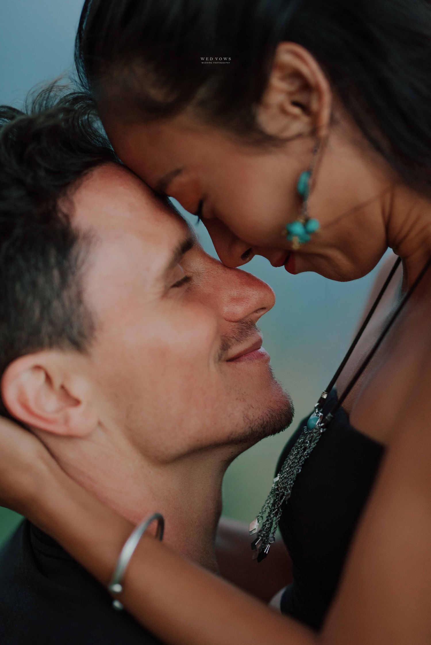 A romantic interracial couple leaning foreheads together, smiling intimately in a tender close-up portrait.