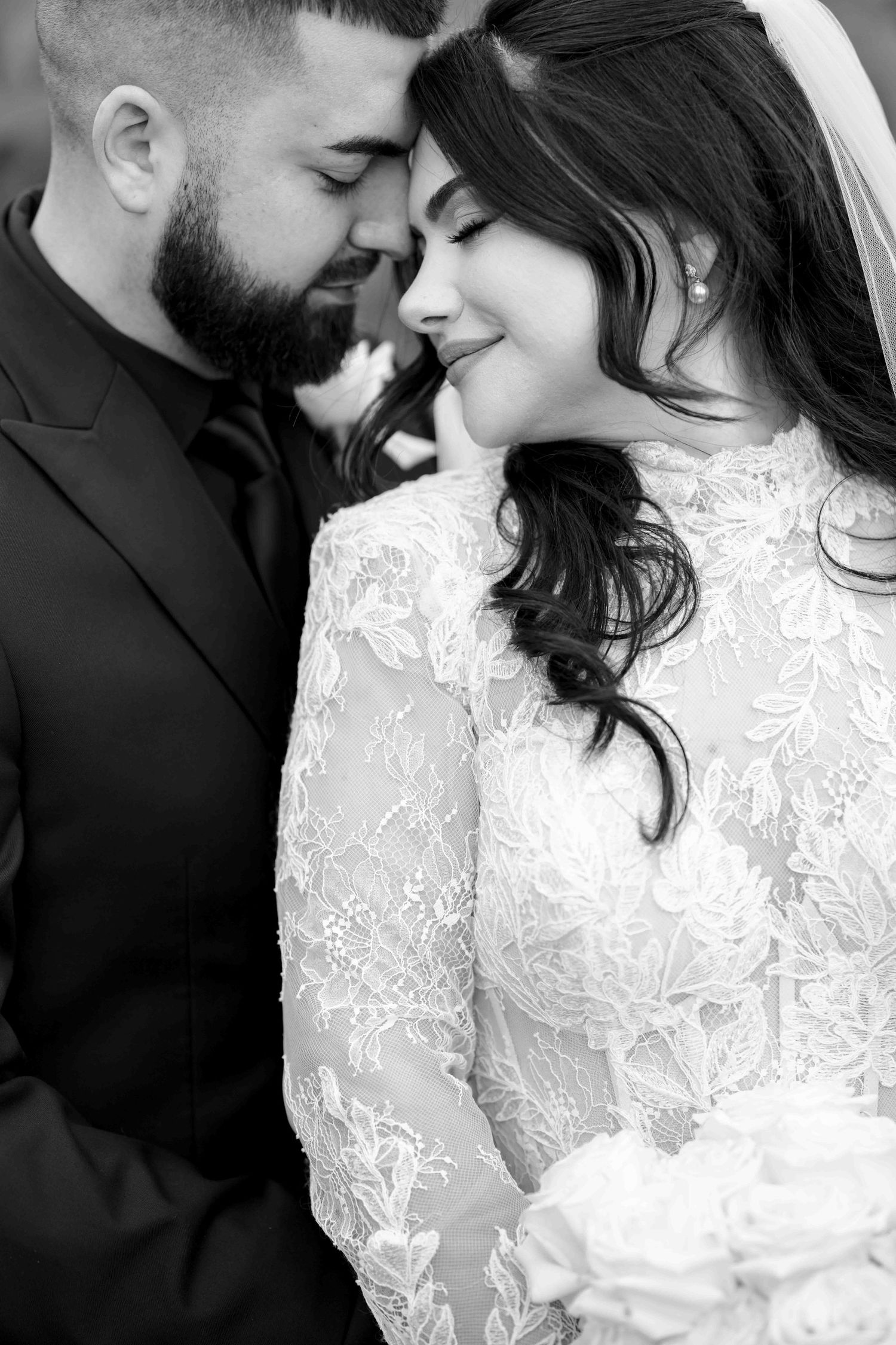 Intimate black and white close-up of bride and groom touching foreheads tenderly on their wedding day.