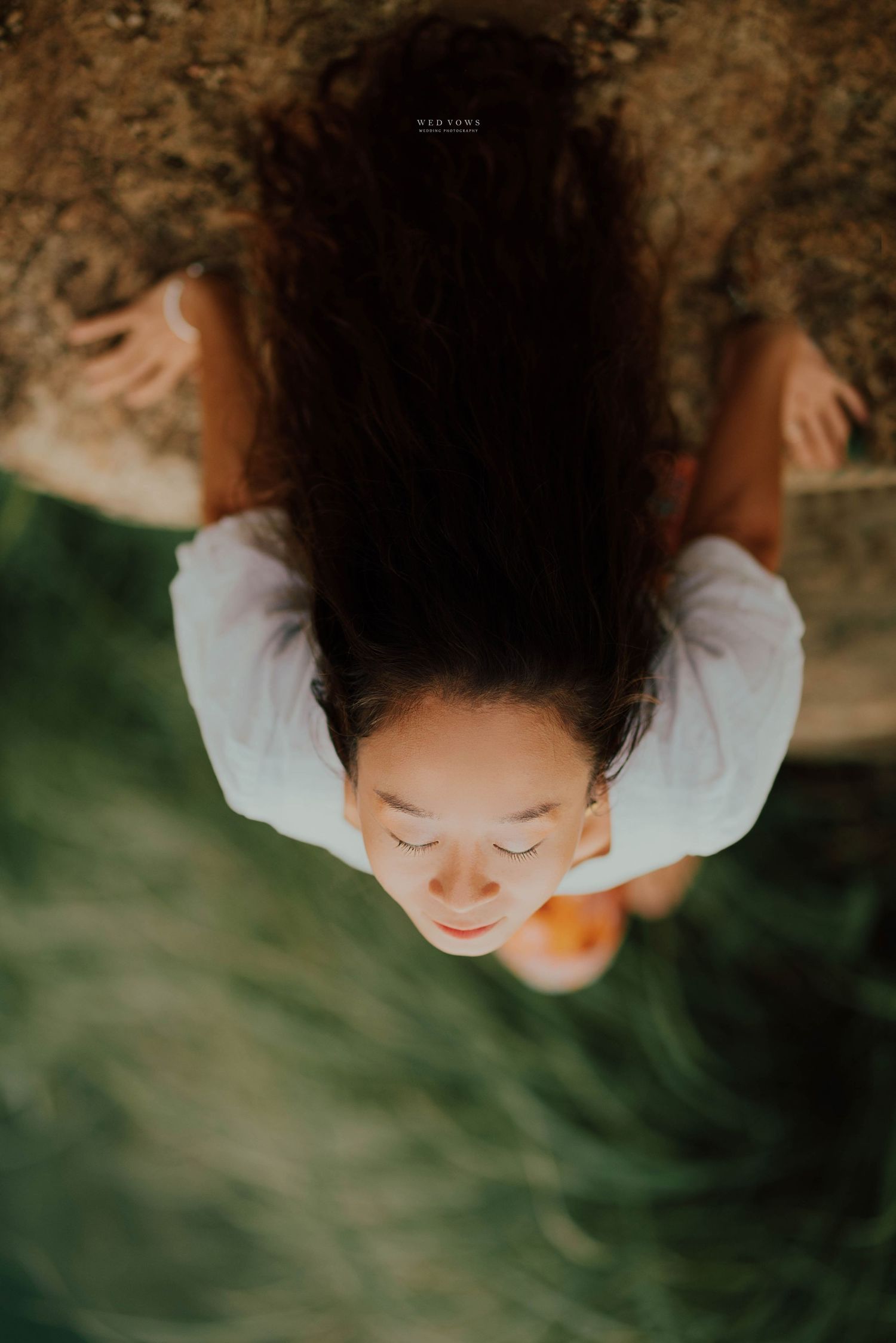 Aerial view of young woman with curly hair sitting peacefully on rocky surface.
