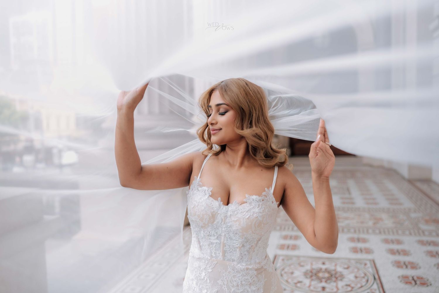 Bride in lace wedding dress holds flowing white veil outdoors on her wedding day.