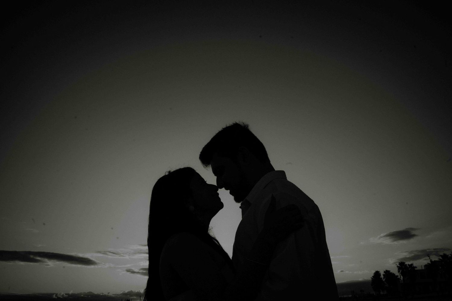Silhouette of a romantic couple facing each other against a dramatic dusk sky.