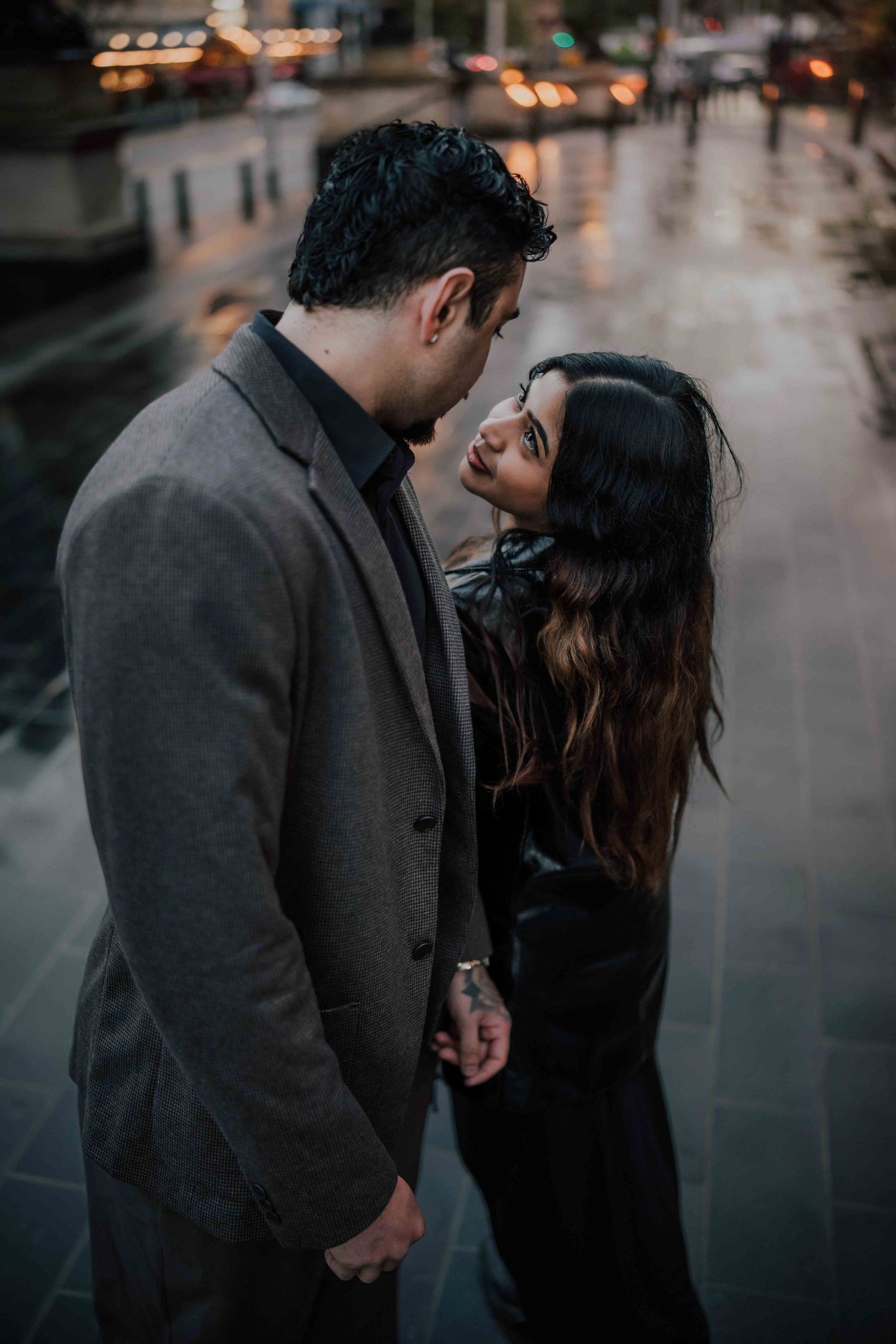 Romantic couple holding hands and gazing at each other on a rainy city street at night.